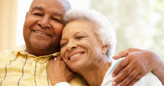 A smiling senior man and woman sit close to each other.