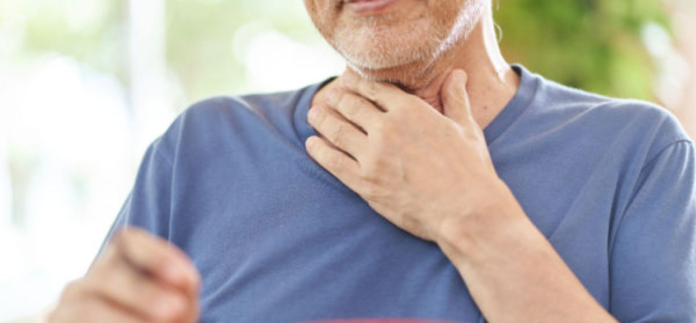 A senior adult with swallowing difficulties, or dysphagia, puts his hand on his neck area as he struggles to swallow.
